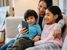 Mother using smart phone while taking selfie with her children at home.