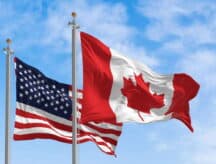 A US and Canadian flag waving in the wind on a semi-cloudy day